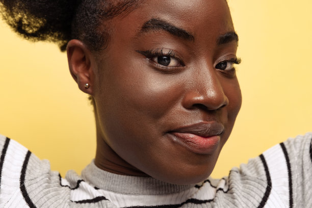 深色皮肤的年轻女孩的特写脸看着相机孤立在紫色霓虹灯的黄色工作室背景。图片下载