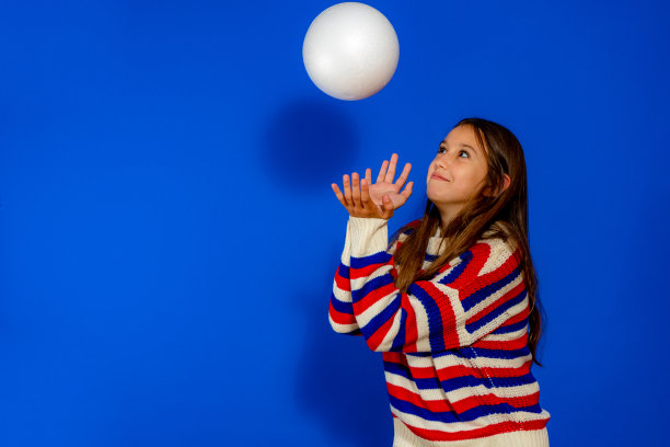 快乐的女孩接住了球。孤立在蓝色背景上图片下载