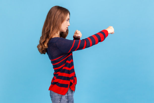 侧面的愤怒好斗的女人穿着条纹休闲风格的毛衣，握紧拳头，准备进行打击，自卫。图片下载