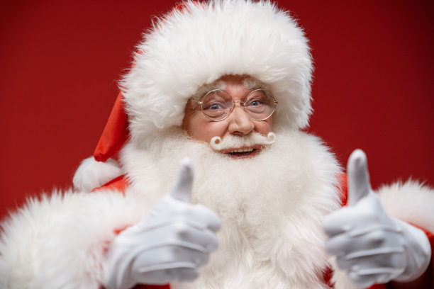 欢乐的圣诞老人的特写镜头在红色背景的相机上竖起大拇指图片下载