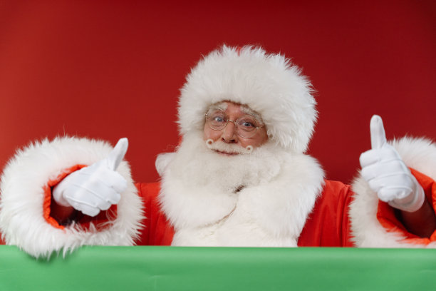 这是一个专业工作室拍摄的迷人的圣诞老人在红色背景上，在他面前的色度键上竖起大拇指图片下载