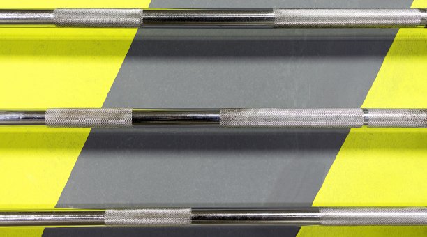 在灰色和黄色线条的墙上，放置着用于举重的铬金属杆图片下载