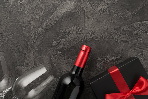 俯视图照片的情人节装饰酒瓶，两个酒杯和黑色礼品盒与红色蝴蝶结在孤立的纹理深灰色混凝土背景与空的空间图片下载