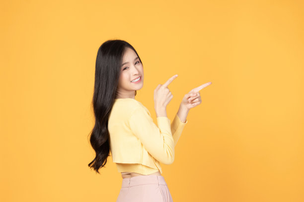 美丽的亚洲女人穿着黄色t恤微笑并指着复制空间孤立在黄色背景工作室肖像。图片下载