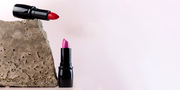 旗帜红色和粉红色的口红在开放的管和灰色的石头在粉红色的背景图片下载