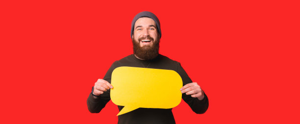 横幅大小的照片微笑的年轻男子与胡子持有空白的黄色演讲泡沫图片下载