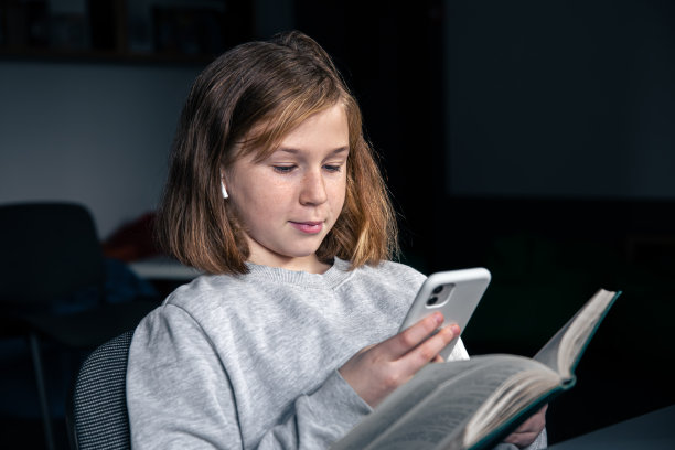 一个十几岁的女孩用智能手机而不是看书。图片下载