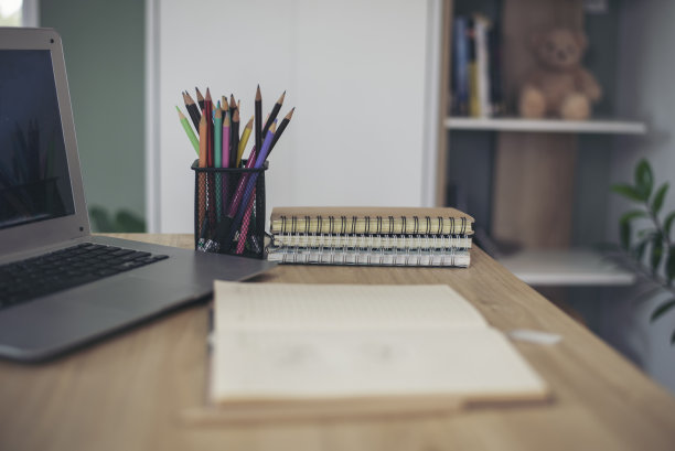 学生概念课桌。笔记本电脑用于备考，书放在课桌上供学生在家网上作业。桌上型笔记本电脑，笔记本，书和铅笔放在木制的桌子上。图片下载