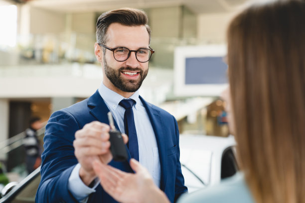 一个穿着正装的英俊白人男性店员在买完新车后给女顾客车钥匙的特写镜头。图片下载