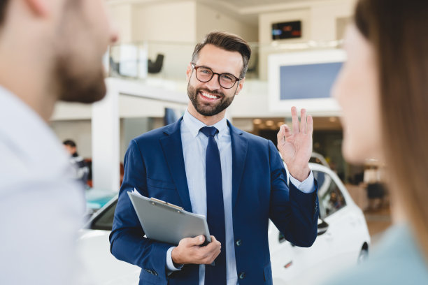 聚焦的照片，年轻的男性店员解释说，提供购买新车的白人家庭年轻的丈夫和妻子在汽车经销商店显示良好的姿态。图片下载