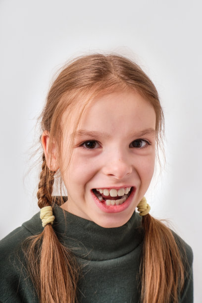 肖像微笑的9岁女孩与一个缺失的乳牙在牙龈。这孩子的乳牙掉了。在一个灰白的背景上。特写镜头图片下载