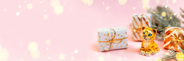老虎象征着2022年的中国新年。云杉树枝老虎雕像和粉色粉彩背景的金色礼盒。副本的空间。横幅素材图片