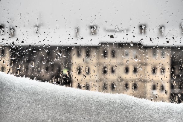 窗外的景色让冬天融雪。融化的雪堆和水滴落在玻璃上。有许多窗户的多层建筑。圣诞新年明信片。忧郁和泪水还是春天的到来图片下载