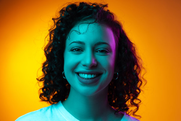 特写年轻美丽开朗的女孩微笑孤立在黄棕色工作室背景霓虹灯。图片下载