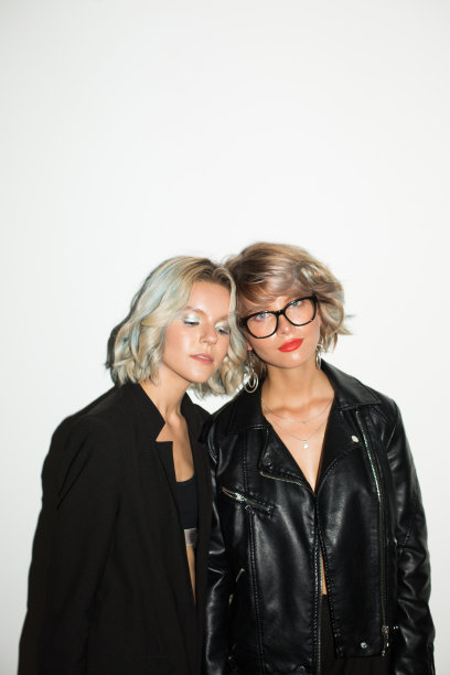 两个美丽的女孩在黑色夹克梦幻地看着相机在白色的背景花时间在一起图片下载