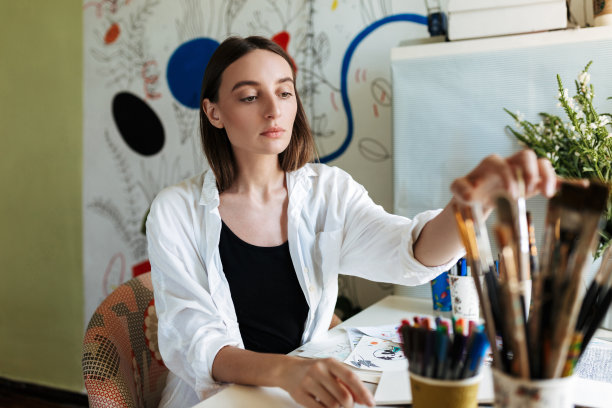 年轻的画家在书桌深思选择油漆刷在创造性的工作场所在家里图片下载