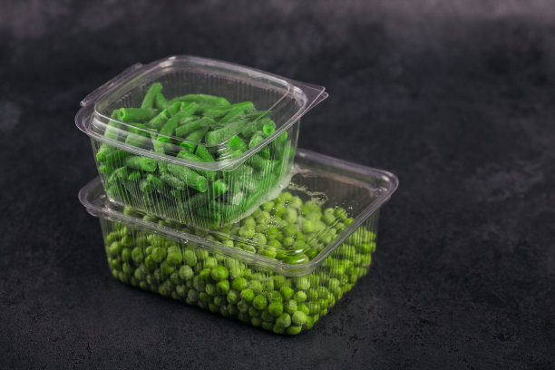 黑色的桌子上放着塑料容器，里面放着不同种类的有机速冻蔬菜。绿豌豆和切好的青豆放在盒子里图片下载