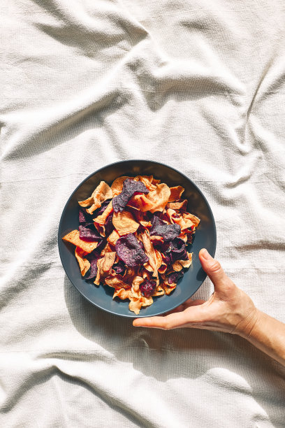 手拿一个盛着脆脆的蔬菜片的盘子放在铺着亚麻布桌布的桌子上。素食点心。选择健康饮食。适当的营养。脱水蔬菜图片下载