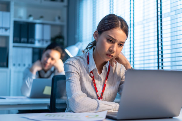 疲惫的亚洲生病的商业女工在办公室的桌子上工作。工作繁忙的员工会因为熬夜和加班而感到疲惫头疼，晚上在工作场所的电脑桌前整理工作文件。图片下载