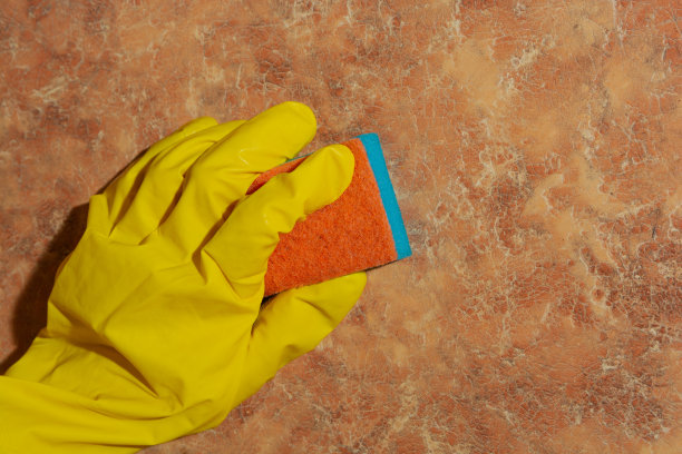 一位戴着黄色手套的妇女在用海绵清洗厨房的墙壁。打扫屋子的概念图片下载