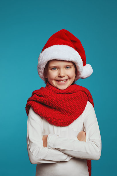 兴高采烈的小女孩戴着圣诞帽和红围巾，看着镜头图片下载