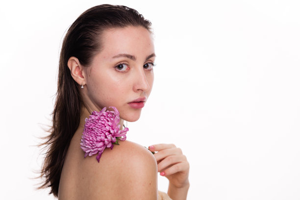 可爱的年轻女子，肩膀上有朵花，靠近脸。赤裸的肩膀，清澈的皮肤。皮肤护理和水疗概念在白色背景。看相机的女人图片下载