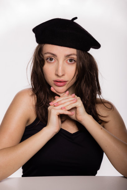 肖像华丽年轻的时尚模特在黑色贝雷帽摆姿势靠在桌子上的白色背景。特写年轻美丽的女人与健康干净的皮肤图片下载