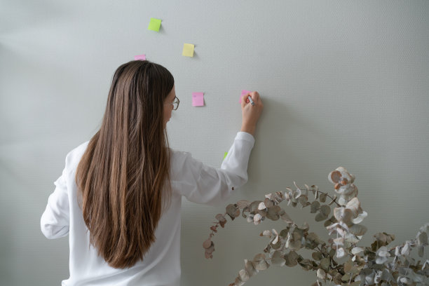 染了一头漂亮头发的女人靠墙站着，在彩色贴纸上写字。业务规划图片下载