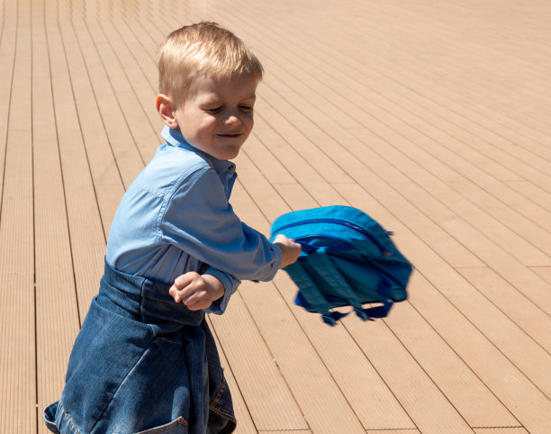 心满意足的男孩手里拿着一个背包。阳光明媚的一天。有选择性的重点。有关学童的文章图片。图片下载