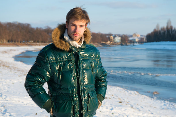 一个家伙在寒冷的冬天穿着带兜帽的夹克。抗风的衣服。冬季时尚男装。冬天的衣服。男人大胡子站暖夹克雪自然背景。时髦的冬季时装图片下载