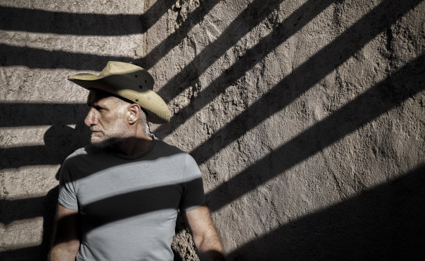 在一个有阳光和阴影的废弃房子里，戴着牛仔帽的成年男子的肖像图片下载