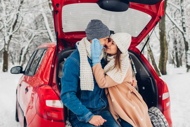 在冰雪覆盖的冬天森林里，情侣们在汽车后备箱里拥抱。人们在公路旅行期间在户外放松图片下载