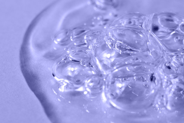 透明的面部血清与泡沫在浅紫色背景宏。透明质酸液体泡沫凝胶特写。2022年的颜色非常接近。保湿美容产品质地。图片下载