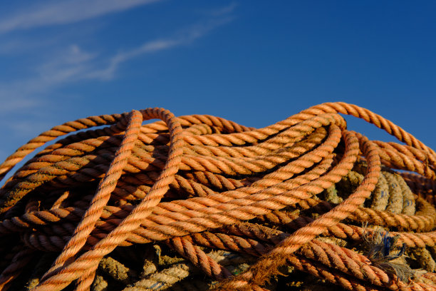 近距离拍摄浅棕色磨损的渔船绳索在蓝天下的海滩上。图片下载