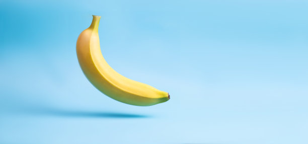 香蕉悬浮。蓝色背景上的一整根黄色香蕉。放置你的文本。图片下载