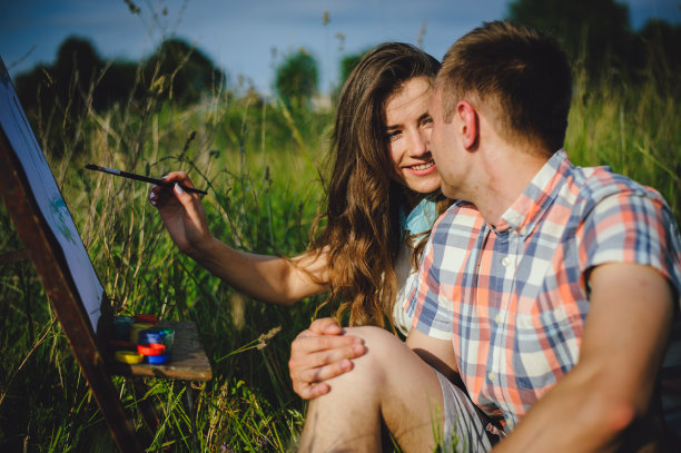 一对在城外度假的艺术家情侣。爱情故事。一个美丽的女孩对她的男朋友微笑的肖像。图片下载