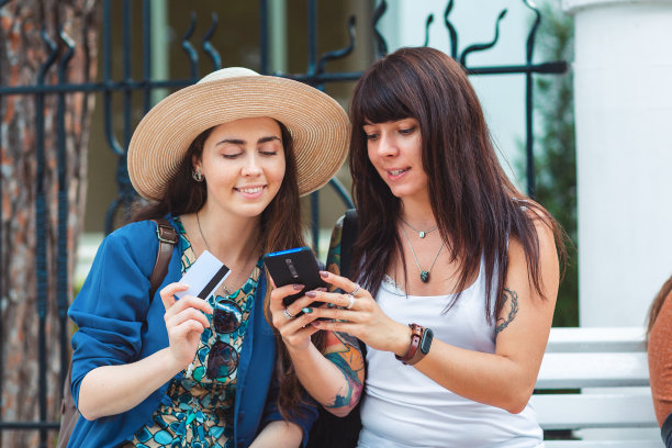 两名女子坐在街上，微笑着看着自己的智能手机，在网上购物。通信与现代技术的概念图片下载