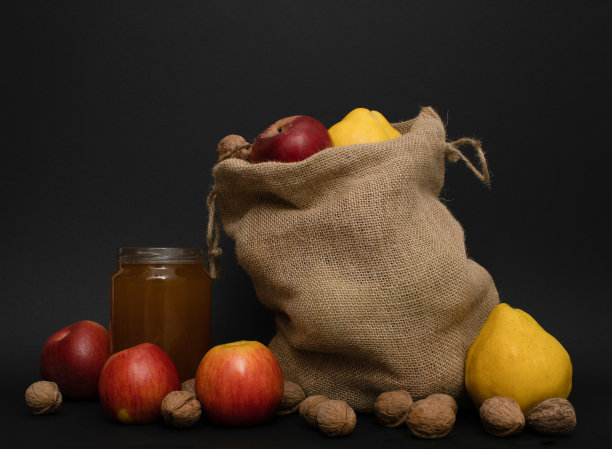 陈年黄麻袋与蜂蜜在罐子里，苹果，核桃和苹果榅桲在黑色的背景。地中海传统圣诞作文图片下载