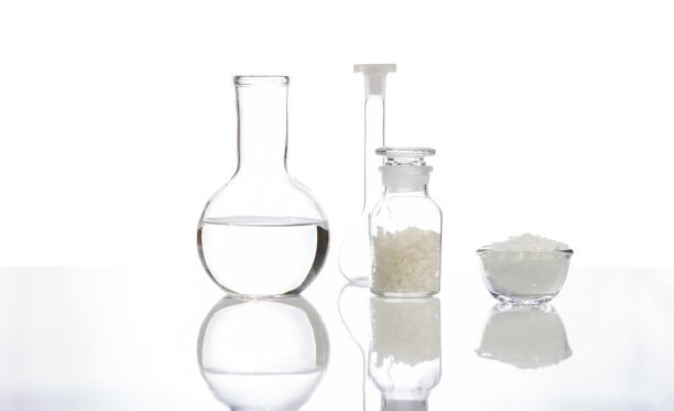 白色片状化学物质在玻璃容器中放置在化学试剂瓶玻璃中的海盐旁边，水晶透明液体在平底烧瓶和容量瓶中。侧视图图片下载