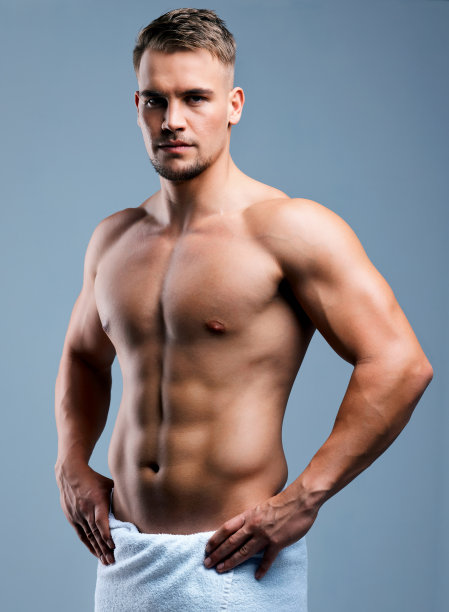 一个肌肉发达的年轻男子在一个灰色的背景下，拿着毛巾摆姿势图片下载