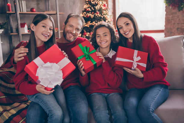 照片可爱的家庭拥抱持有礼物坐在沙发上穿红色毛衣牛仔裤在室内的圣诞夜图片下载