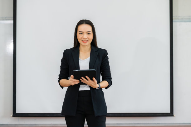 一名亚洲教师在空荡荡的大学教室前举着平板电脑。孤立的背景图片下载