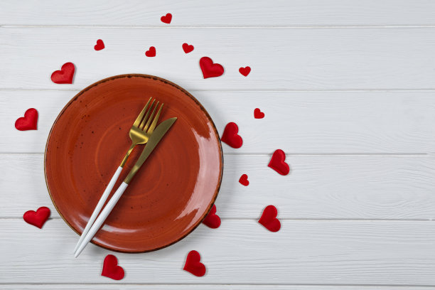 情人节餐桌设置在白色木制背景顶部视图，照片与copyspace。一个红色的盘子，金色的餐具和红心顶视图，浪漫的晚餐概念图片下载