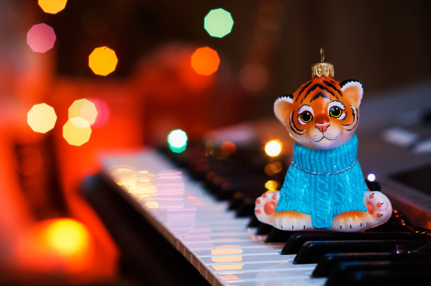 2022. 虎年。春节快乐。圣诞树玩具在钢琴键上。电子花环上的彩色灯光反射在乐器的键盘上。图片下载