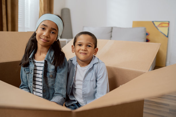 兄弟姐妹微笑地坐在一个空纸箱在搬家，孩子们躲他们的父母，闲逛，玩，姐妹和兄弟喜欢为他们的新家打包东西图片下载