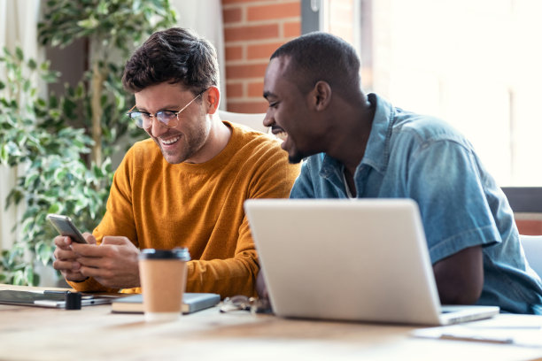 两个平面设计师在现代初创公司办公室休息，同时看有趣的东西在移动电话在一起。图片下载