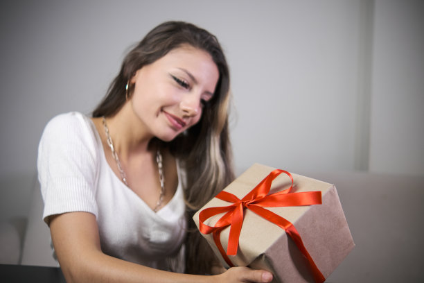 微笑的女人拿着用牛皮纸包着红丝带的礼盒，室内照片图片下载