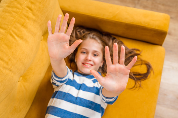 一个美丽的金发小女孩微笑着躺在黄色沙发上的特写，一张照片在她的上面图片下载