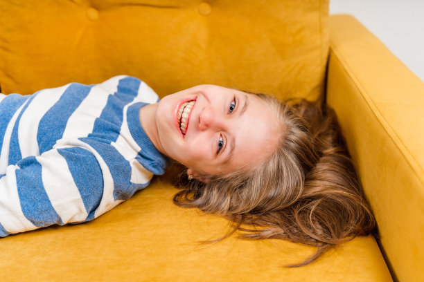 一个美丽的金发小女孩微笑着躺在黄色沙发上的特写，一张照片在她的上面图片下载