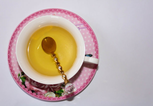 一个金色的茶匙在一个茶杯和一个彩色的茶碟的特写;俯视图;白色背景图片下载